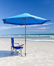 A bright beach umbrella casting shade over a sandy shore with waves in the background.