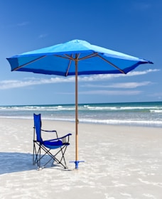 A bright beach umbrella casting shade over a sandy shore with waves in the background.