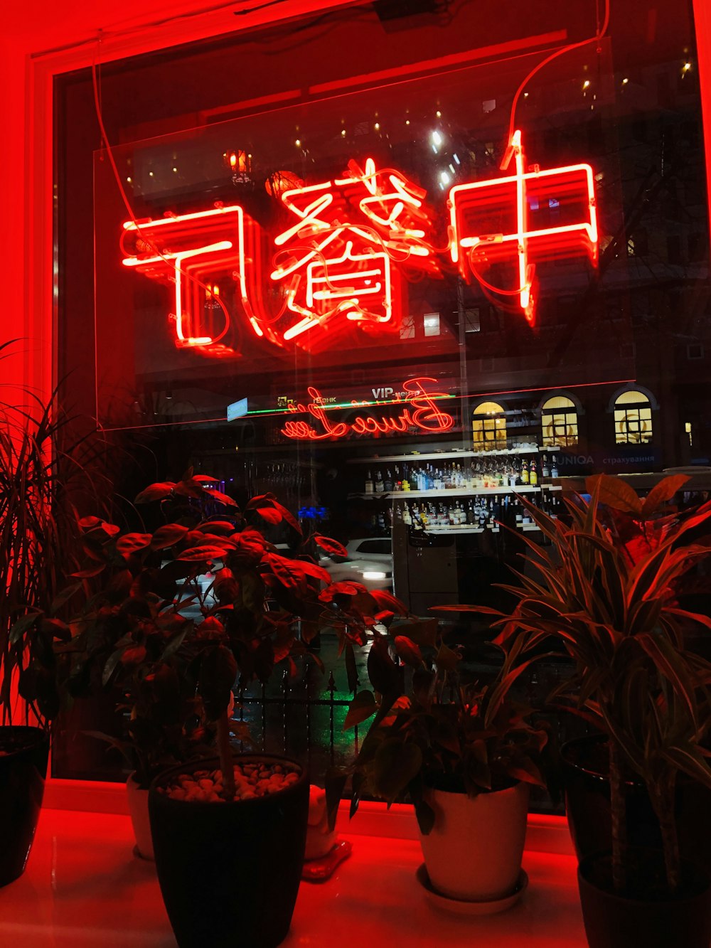 a red neon sign above a restaurant with potted plants