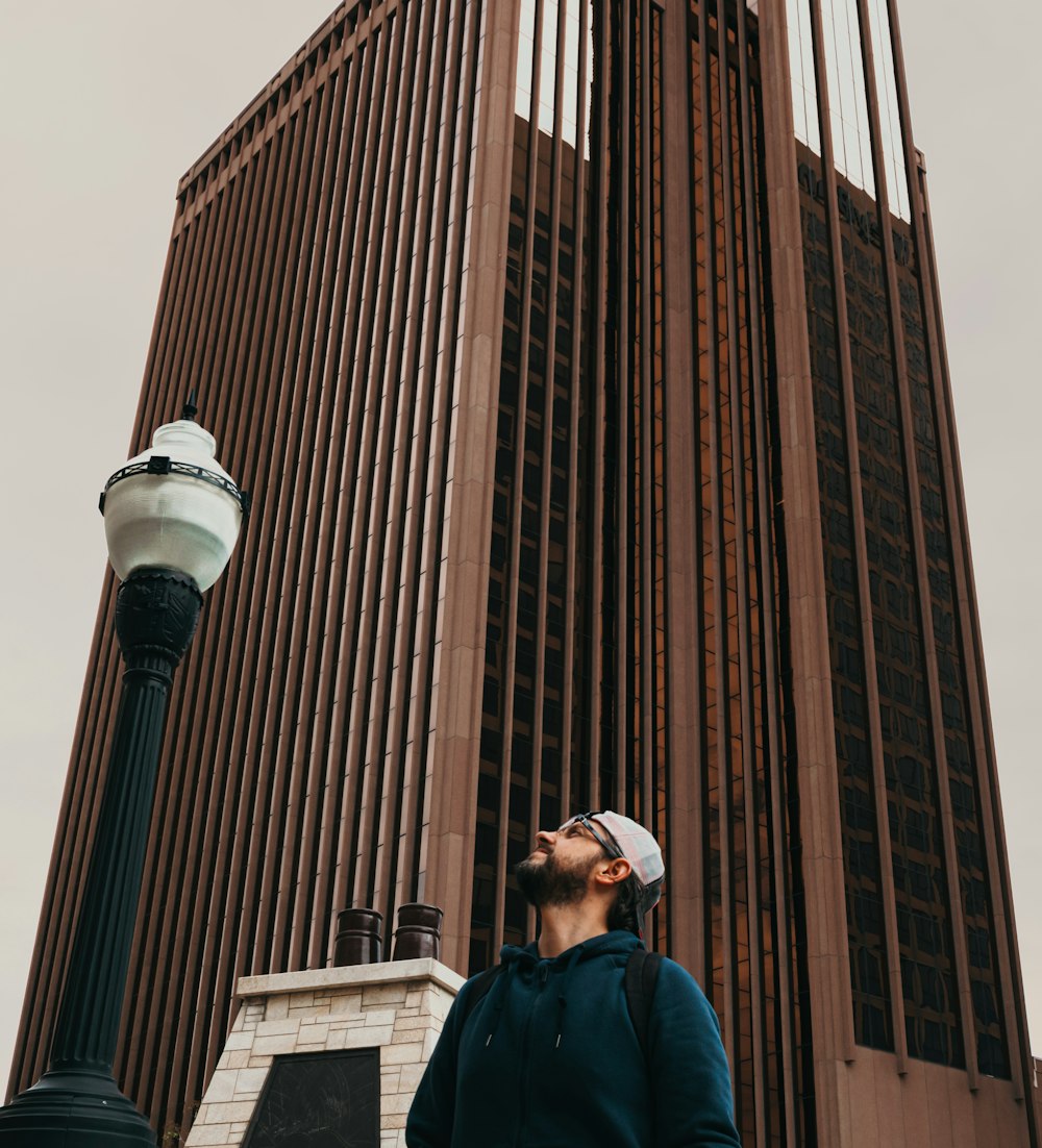 Hombre con chaqueta azul parado cerca de un edificio de concreto marrón durante el día
