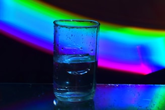 A clear glass of purified water with droplets on the outside, set against a bright, natural background.