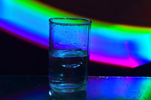 A clear glass of water sparkling under sunlight, with a magnetic device attached to the pipe in the background.