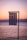 A Greek flag is gently waving in the foreground against a serene backdrop of a calm sea and a pastel-colored sunset sky. The horizon shows a faint outline of distant mountains bathed in soft evening light.