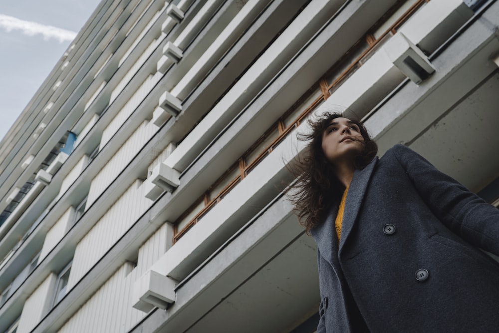 woman in black coat standing near white window blinds