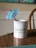 A white mug with a green and blue logo and the words 'GoWP Create Happiness' printed on it sits on a wooden table. A blue cocktail umbrella and a pink straw are placed inside the mug.