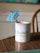 A white mug with a green and blue logo and the words 'GoWP Create Happiness' printed on it sits on a wooden table. A blue cocktail umbrella and a pink straw are placed inside the mug.