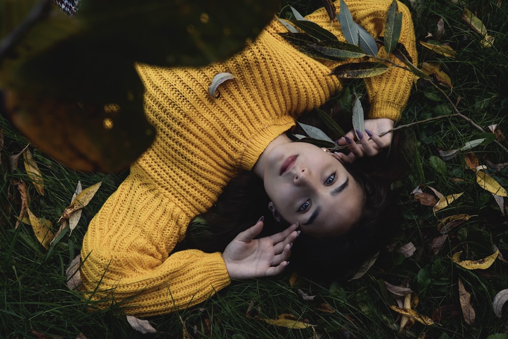 woman in yellow knit sweater lying on green grass