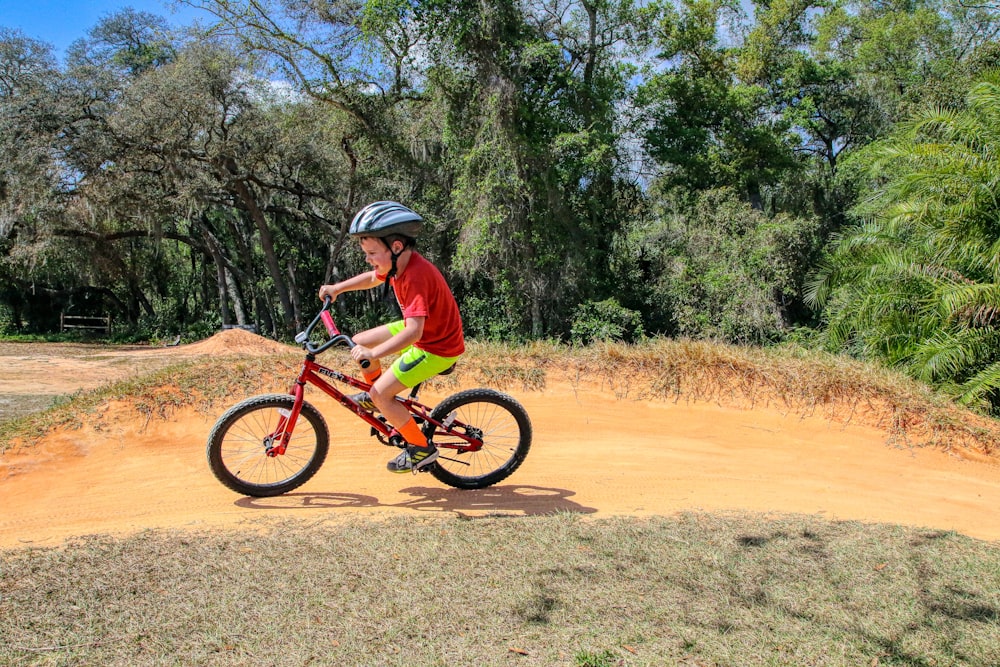 man in green shirt riding red bicycle on brown dirt road during daytime