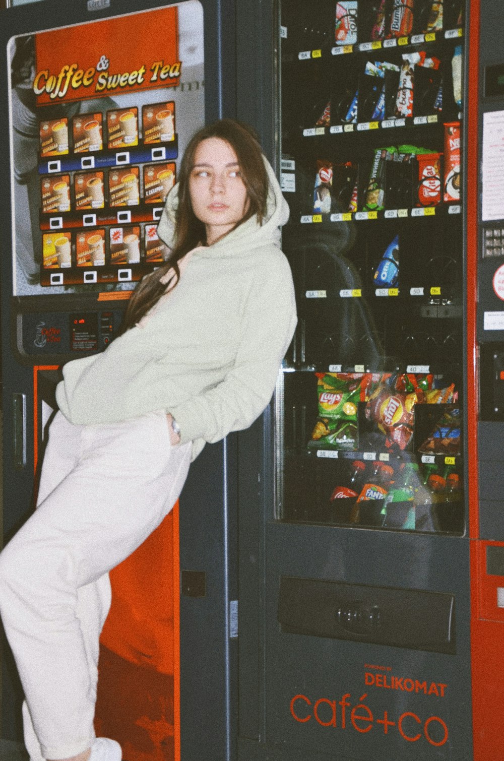 Donna in felpa con cappuccio bianca in piedi vicino a un distributore automatico nero e rosso