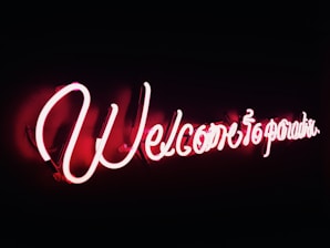 A cozy room softly lit by a vibrant pink neon sign that reads 'Welcome Home.'