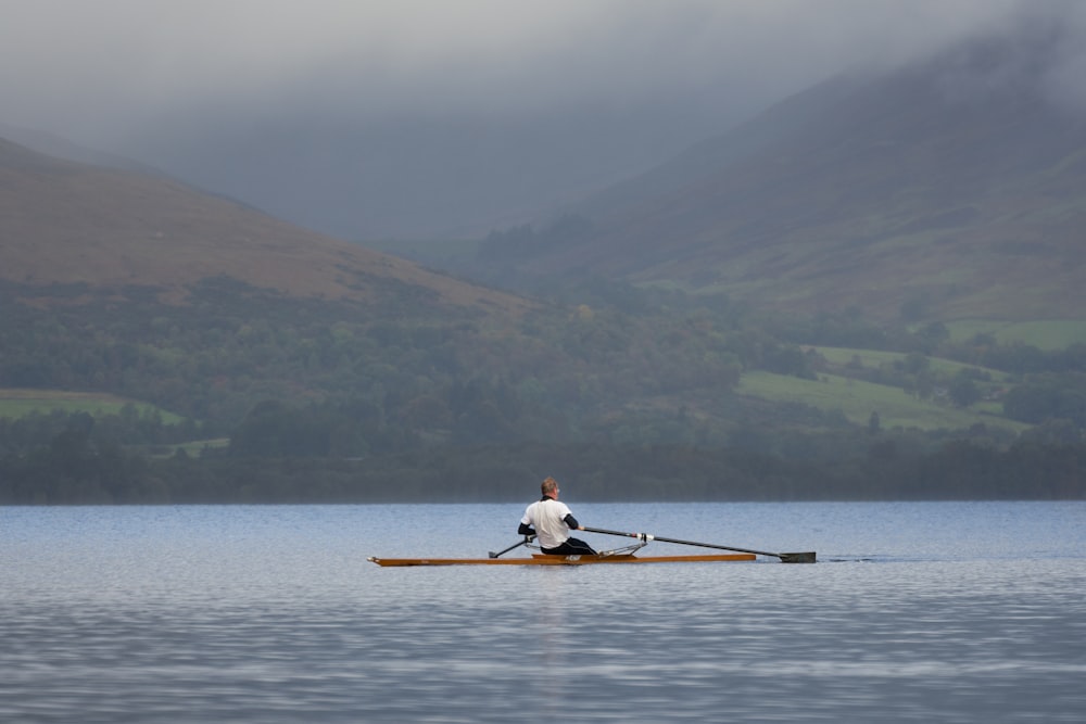 Uomo in camicia bianca che cavalca sul kayak bianco sul lago durante il giorno