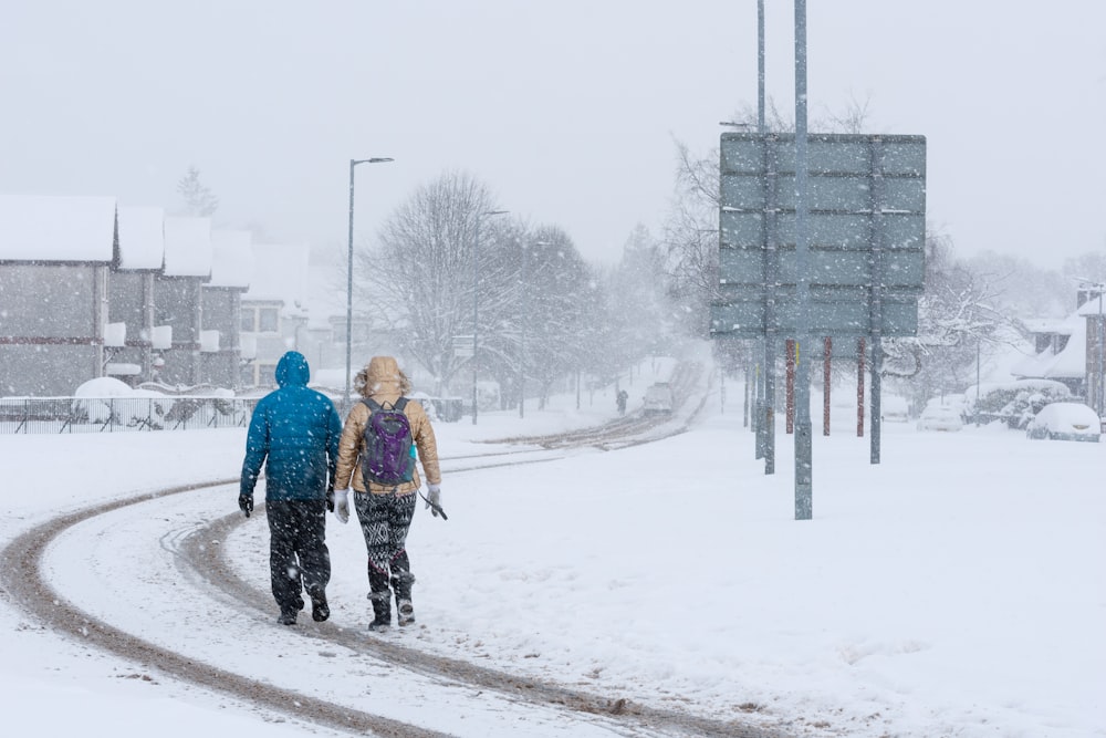 2 person walking on snow covered road during daytime