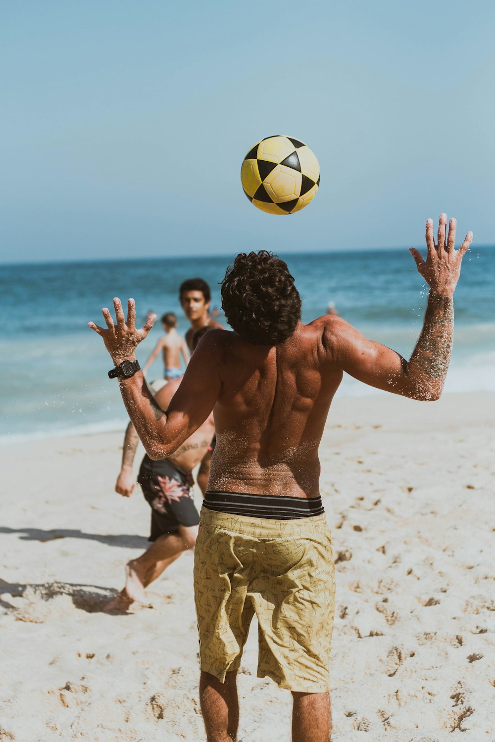 man in yellow shorts holding yellow and black soccer ball on beach during daytime