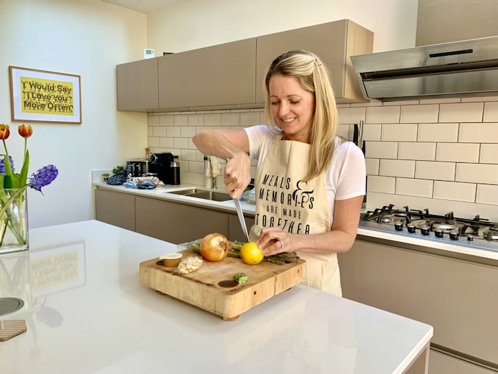 A smiling woman wearing an apron cleaning a bright kitchen.