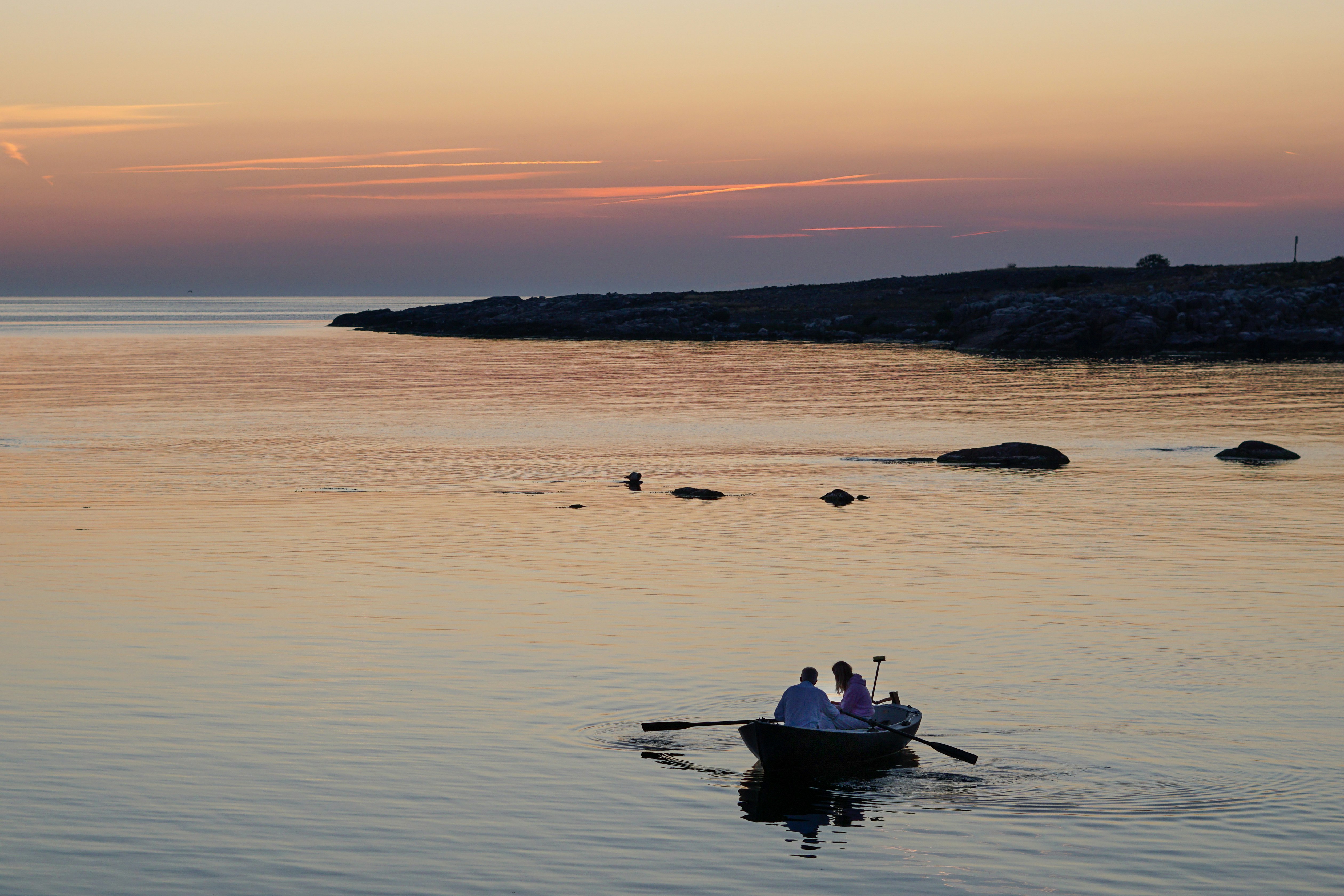 silhouette of 2 people riding on boat on sea during sunset