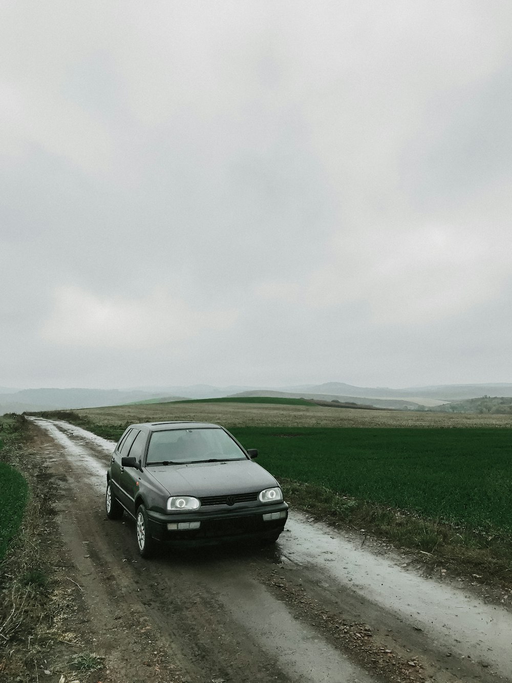 black car on road near green grass field under white sky during daytime