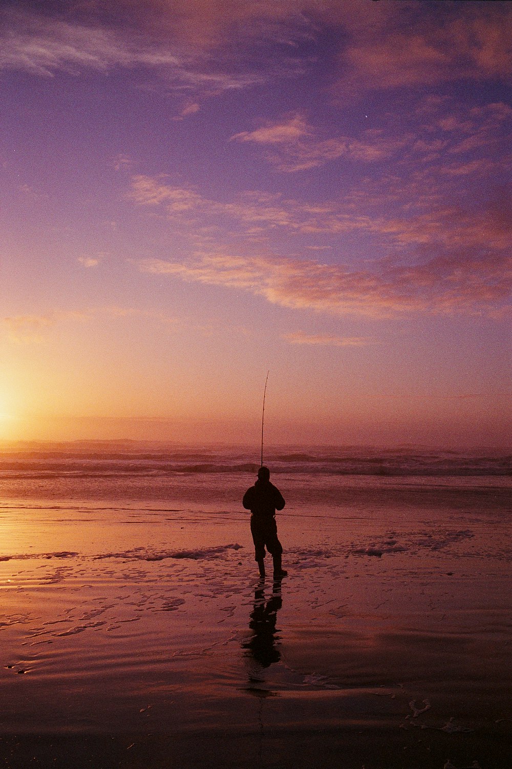 silhouette of man holding fishing rod during sunset