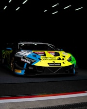Close-up of a sleek race car adorned with vibrant sponsor logos under bright track lights.