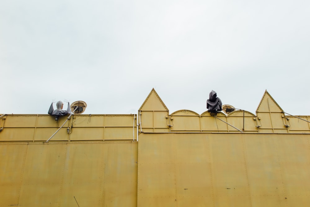 man in black jacket sitting on yellow building