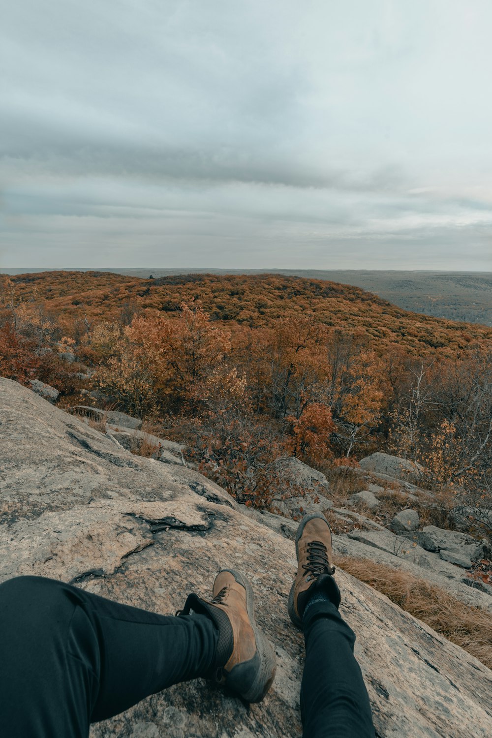 person in black pants and brown hiking shoes sitting on rock during daytime