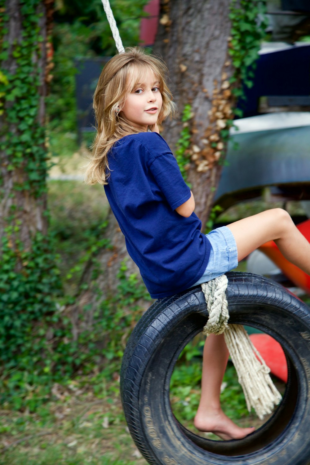 girl in blue long sleeve shirt and blue denim shorts sitting on tire swing