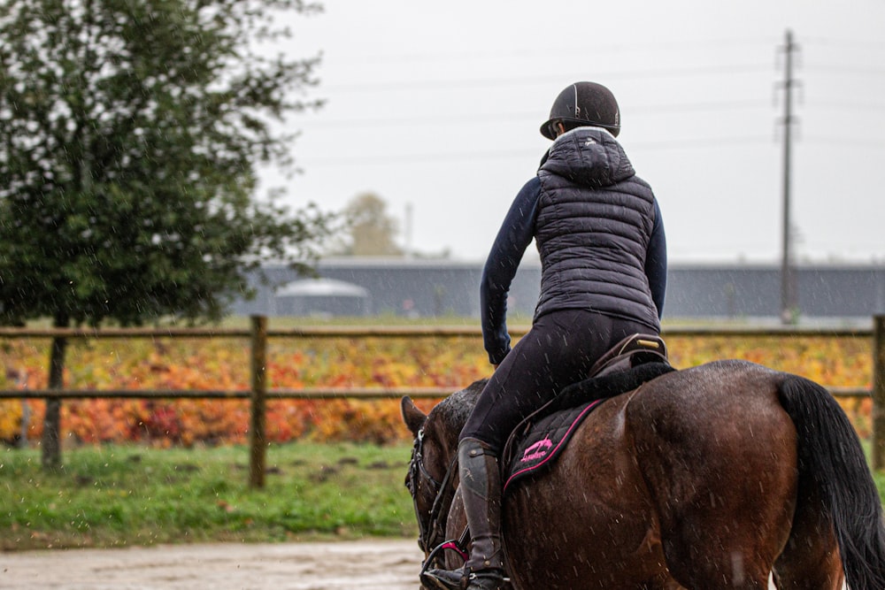 Homme en veste noire chevauchant un cheval brun pendant la journée