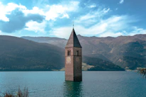 Close-up of the ancient bell tower standing proudly in the middle of Reschensee lake at sunset.