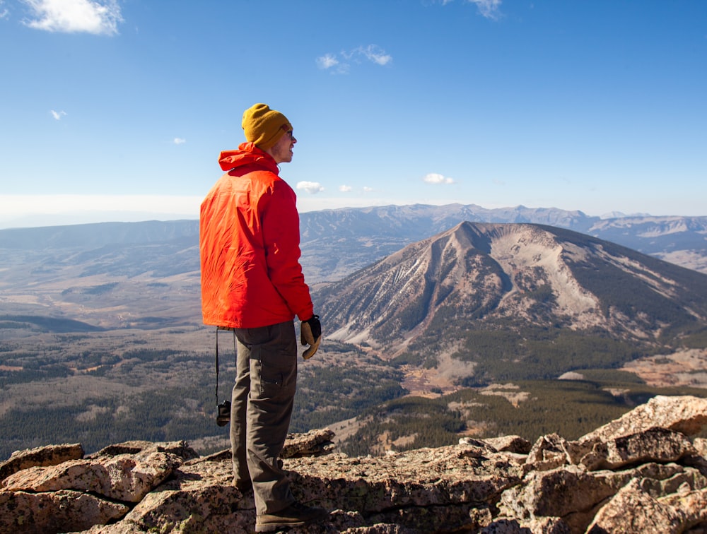 man in orange hoodie standing on rocky mountain during daytime