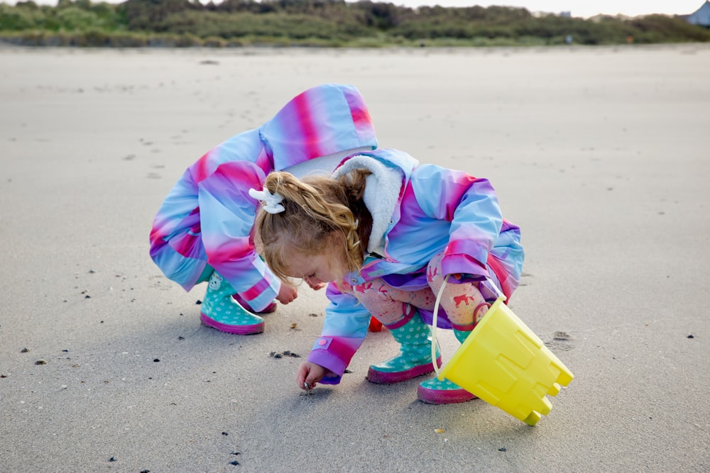 girl in pink jacket holding yellow plastic bucket on beach during daytime