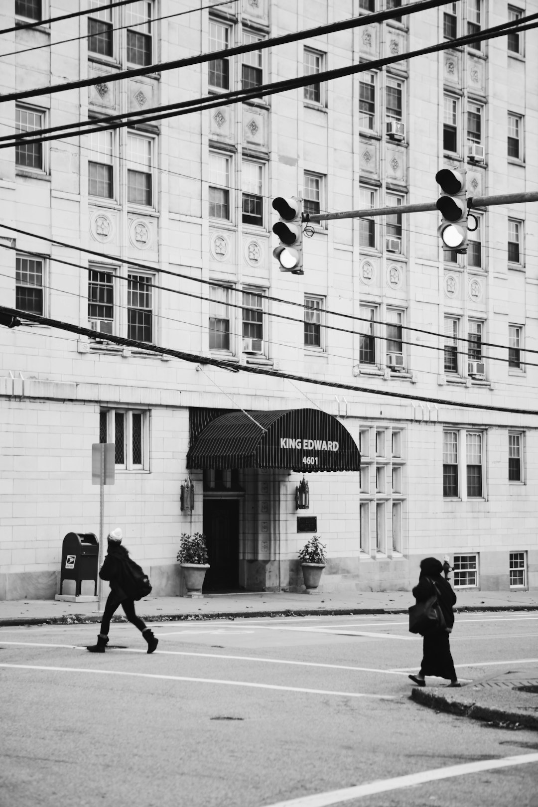 grayscale photo of man walking on sidewalk near building