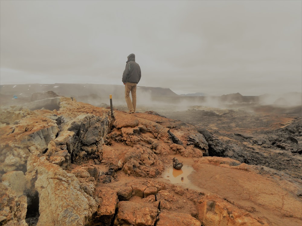 昼間、茶色の岩の上に立っている黒いジャケットの男