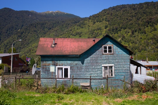 white and red wooden house on green grass field during daytime in Puyuhuapi Chile