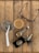 An assortment of everyday items is arranged on a wooden surface. There is a glass of iced coffee with a straw, a pair of eyeglasses, a wristwatch with a gold and silver strap, a key fob with several keys, and a leather wallet with a badge on it.