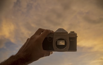 A warm photo of hands holding an old vintage camera against a soft sunset background.