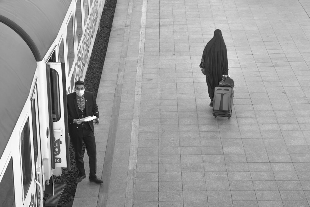 grayscale photo of woman in black hijab standing beside train