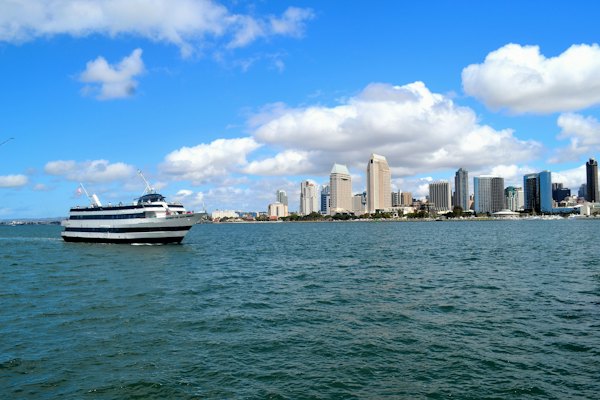 White and black boat on sea near city buildings under blue and white sunny cloudy sky — San Diego, United States