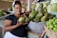 A smiling woman holding a basket of fresh organic vegetables at an outdoor market.