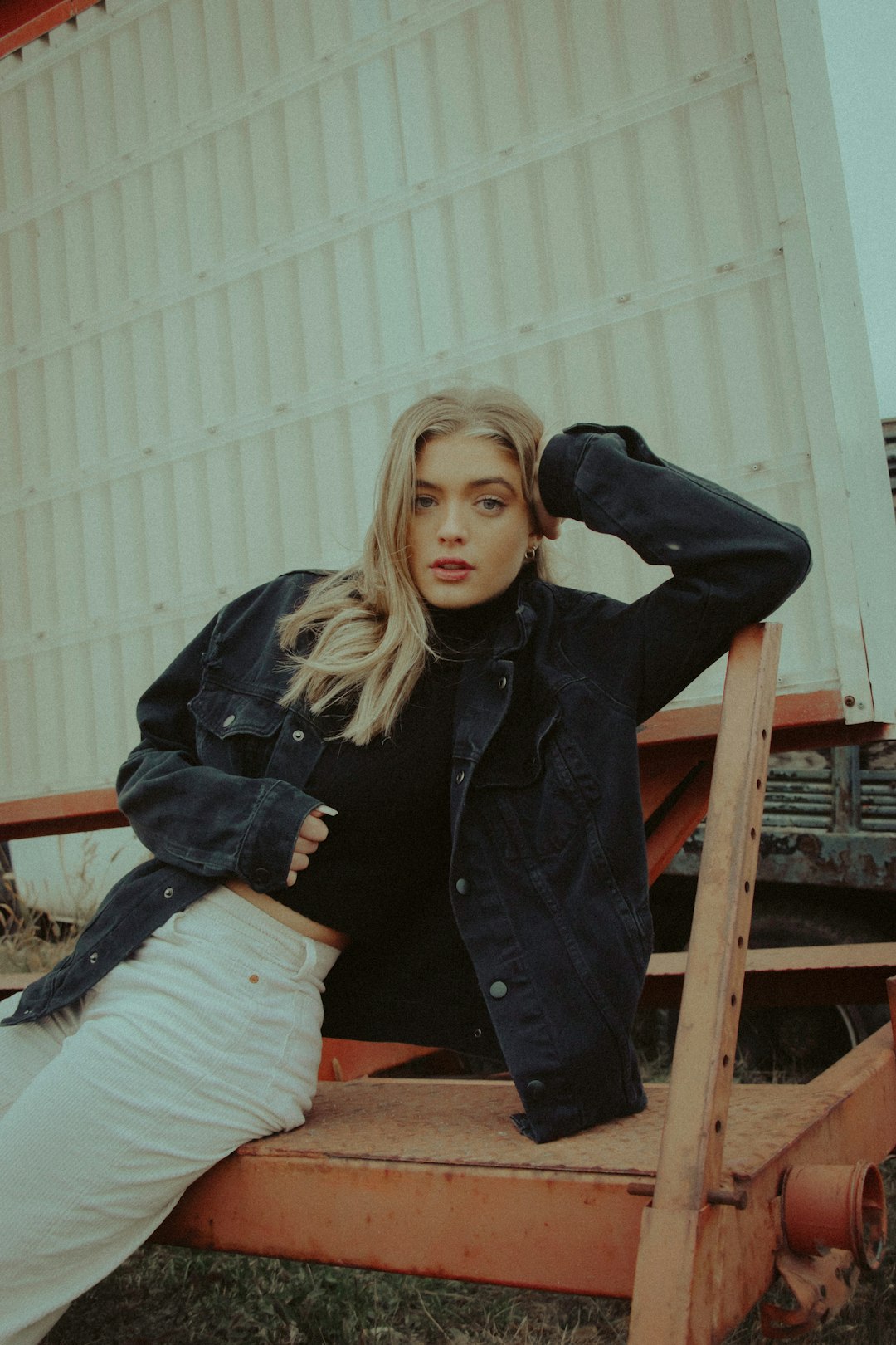 woman in black jacket and white pants sitting on brown wooden ladder