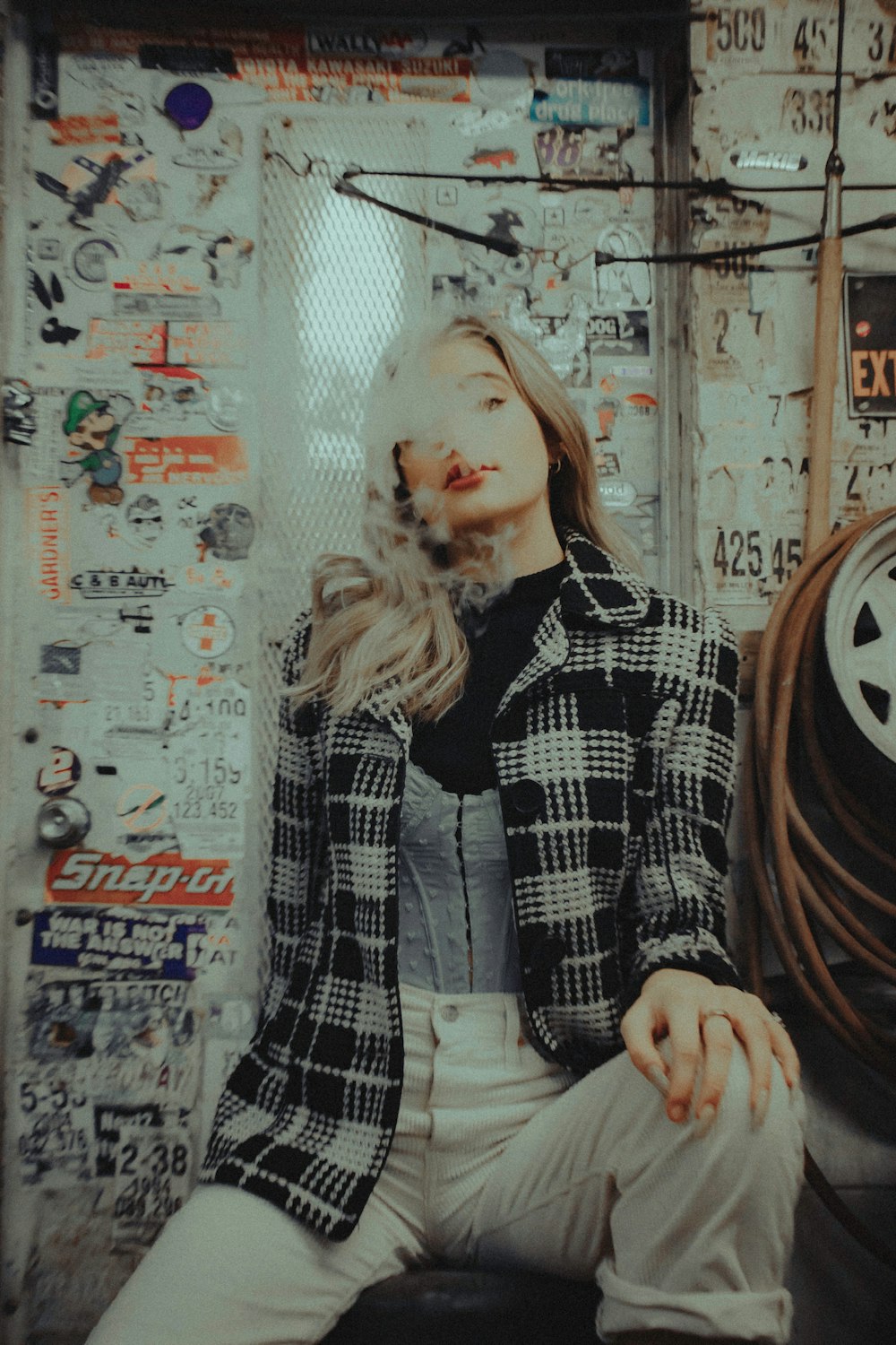 woman in black and white plaid coat standing beside white wall