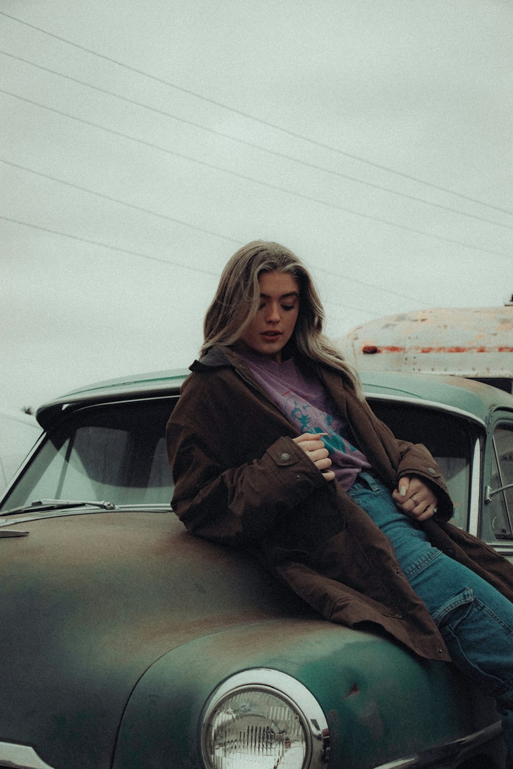 woman in brown coat sitting on car