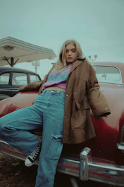 A laid-back scene featuring a plus-size person wearing V8 branded sweatpants beside a classic muscle car.