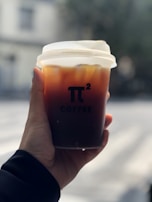 A smiling barista handing a cup of coffee concentrate to a happy customer outdoors.