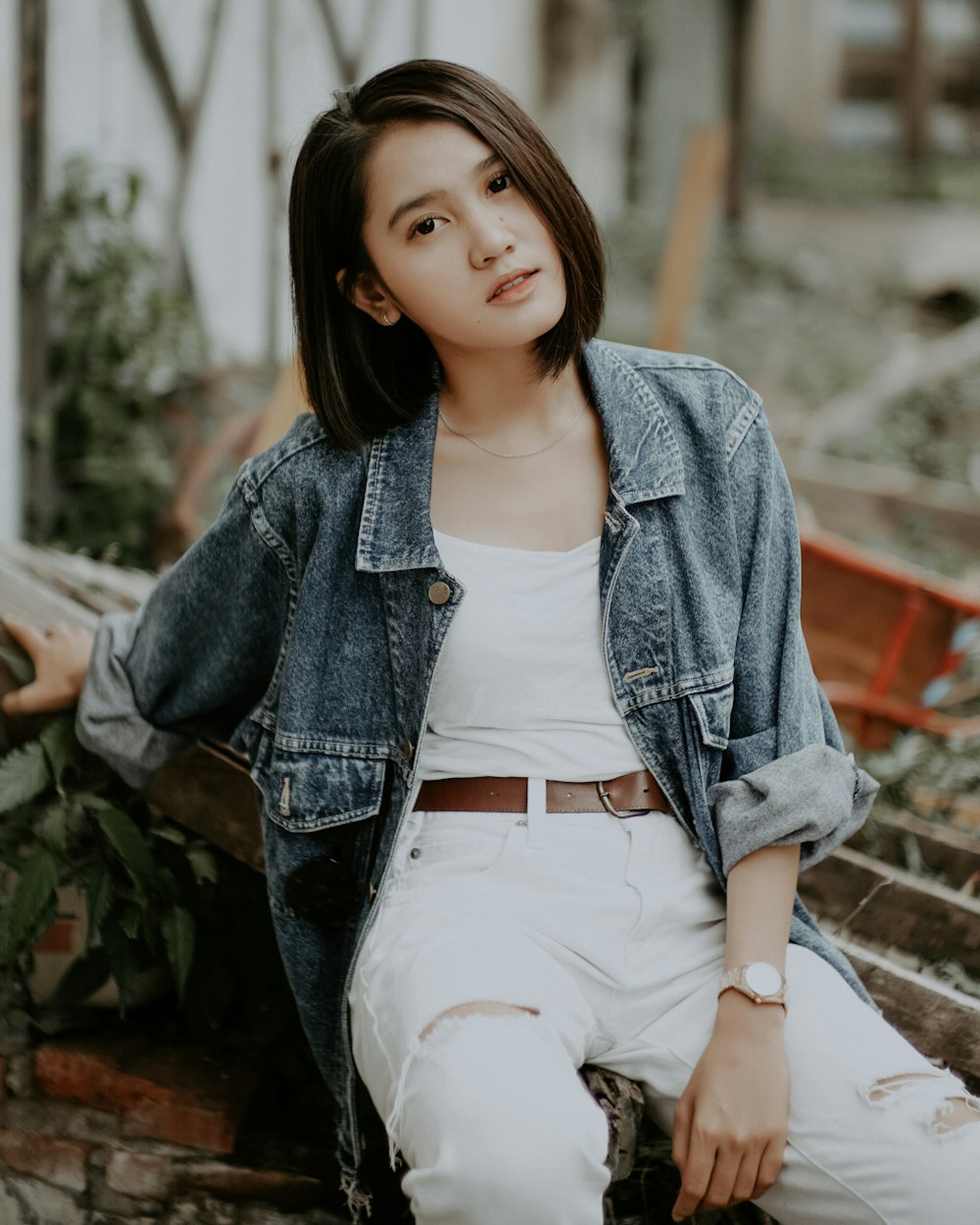 woman in blue denim jacket and white pants sitting on concrete bench during daytime