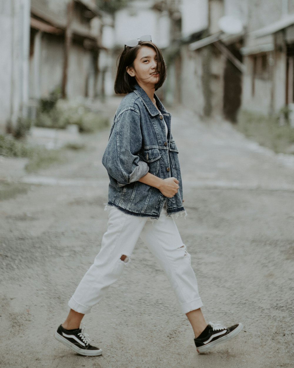 woman in blue denim jacket and white pants standing on gray concrete road during daytime