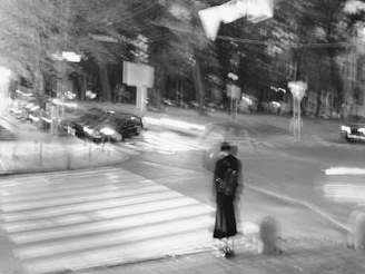 A high-contrast black and white photo of a bustling city street at dusk with blurred motion of pedestrians.