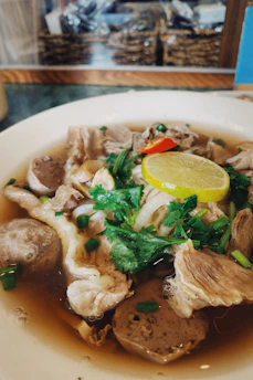 Steaming bowl of beef rib soup garnished with fresh herbs and slices of chili.