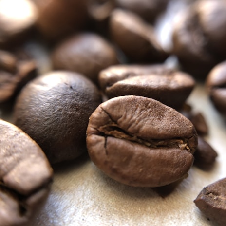 Close-up of fresh coffee beans on a rustic wooden table with natural light highlighting their texture.