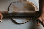 Close-up of hands rolling fresh dough for rotis on a wooden board.