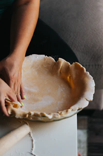 Hands lovingly crimping the edges of a pie crust with fresh ingredients nearby.