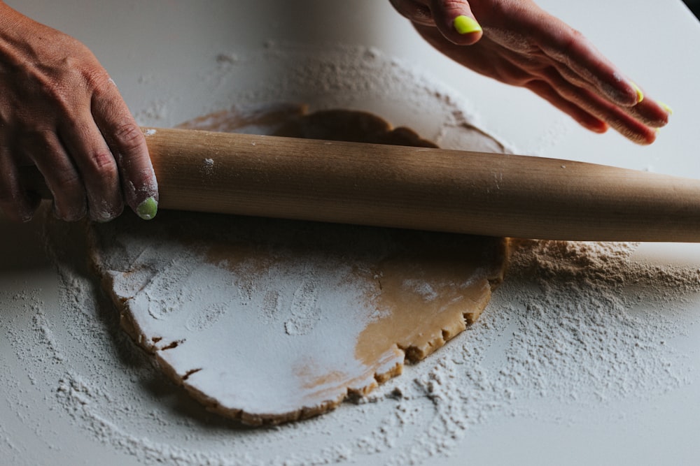 personne tenant un rouleau à pâtisserie en bois brun